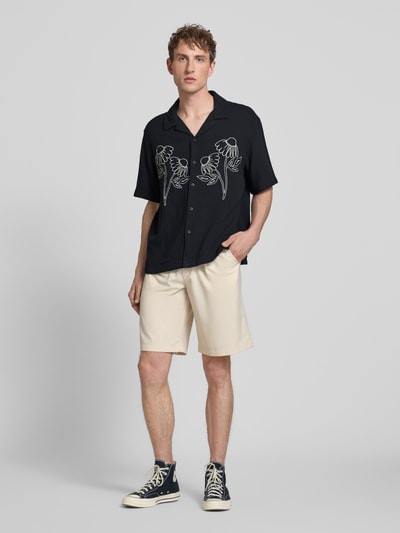 Männermodel trägt Relaxed Fit Freizeithemd aus reiner Baumwolle Modell 'JACKSON' von Only & Sons, Optik: Unifarben, schwarze Seersucker-Struktur, durchgehende Knopfleiste, Stickerei und Kurzarm, Ganzkörperansicht von vorne.
