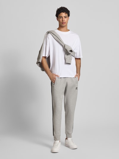 Mannelijk model draagt Sweatpants mit elastischem Bund van adidas Originals in lichtgrijs, katoenmix, loose fit, label-stitching, steekzakken, elastische tailleband, binnenbeenlengte 74 cm, vooraanzicht volledige lengte.