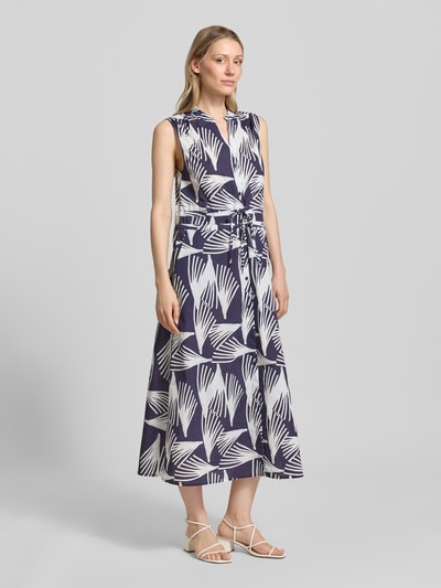 Frauenmodel trägt Hemdblusenkleid mit V-Ausschnitt und Bindegürtel Modell 'Lani' von GUIDO MARIA KRETSCHMER WOMAN, Reine Baumwolle, A-Linie, Allover-Look, Midikleid, Knopfleiste, dunkle und helle Farben, fließende Textur, Ganzkörperansicht von vorne.
