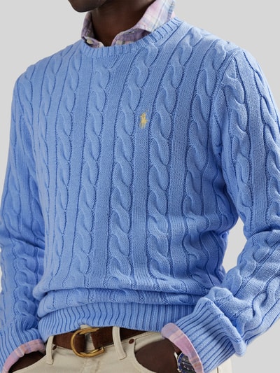 Männermodel trägt Regular Fit Strickpullover aus reiner Baumwolle von Polo Ralph Lauren in Hellblau mit Zopfmuster, Logo-Detail, Nahaufnahme Oberkörper.