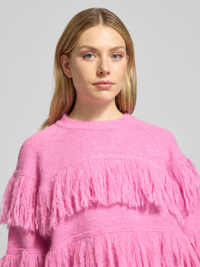 Frauenmodel trägt Relaxed Fit Strickpullover mit Woll-Anteil Modell 'JOHNS' von Essentiel Antwerp in Melange-Optik mit Fransen-Applikationen, Crew Neck, Raglanärmel, geripptem Ärmel- und Rumpfabschluss, Materialverarbeitung Rippstrick, Nahaufnahme Oberkörper.