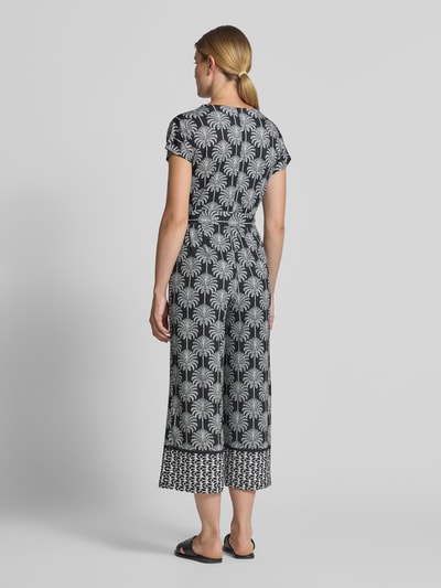 Frauenmodel trägt Jumpsuit mit floralem Allover-Print von MORE, dunkle Grundfarbe mit weißen Blumen, Ganzkörperansicht Rückansicht. Elastischer Material-Mix, taillierte Passform, V-Ausschnitt, kurze Ärmel, Rückenlänge 37 cm, Brustweite 36 cm, Ärmellänge 24 cm, Gesamtlänge 133 cm, Innenbeinlänge 60 cm.