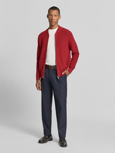 Męski model nosi Strickjacke mit Zweiwege-Reißverschluss und Label-Stitching od Fynch-Hatton w kolorze czerwonym, z bawełny, krój regular fit, stójka, długość tyłu w rozmiarze M 68 cm, długość rękawa 66 cm, widok całej sylwetki od przodu.