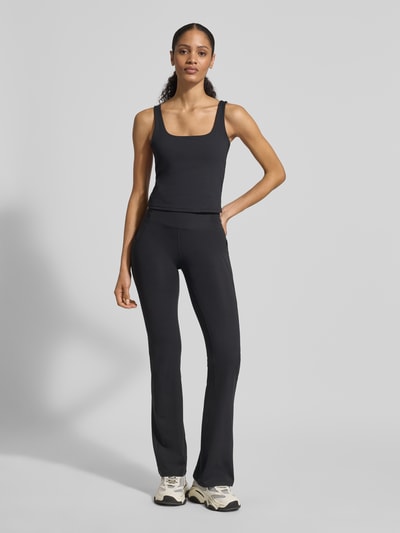 Frauenmodel trägt schwarze Flared Fit Leggins mit Logo-Print Modell 'OASIS' von Fabletics, elastischer Material-Mix, Ganzkörperansicht von vorne.