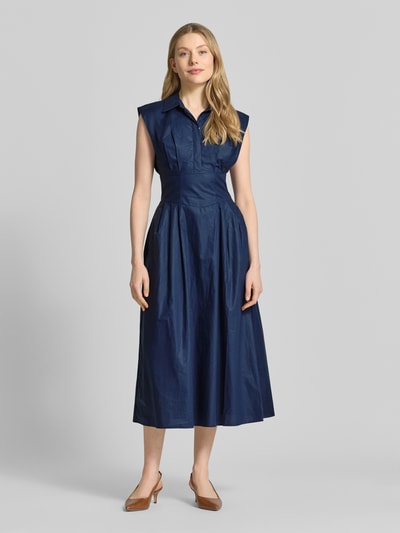 Frauenmodel trägt tailliertes, dunkelblaues Midikleid mit verdeckter Knopfleiste Modell 'CHERRY' von Guess, reine Baumwolle, Hemdblusenkragen, Kappärmel, Ganzkörperansicht von vorne.