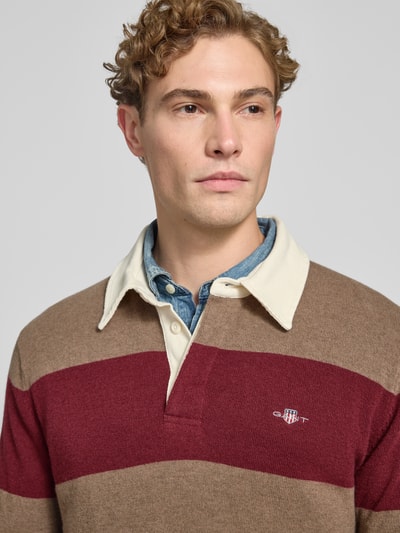 Männermodel trägt Regular Fit Pullover aus reiner Baumwolle von GANT, breite Streifen in Beige und Dunkelrot, Nahaufnahme Oberkörper.