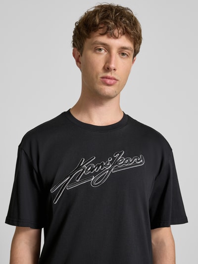 Männermodel trägt Oversized Fit T-Shirt mit Logo-Stitching von KARL KANI, schwarze Farbe, Reine Baumwolle, Rundhalsausschnitt, Nahaufnahme Oberkörper, Rückenlänge bei Größe M: 72 cm.