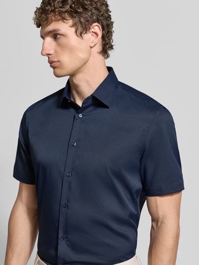 Męski model nosi Slim Fit Business-Hemd mit Kentkragen od Jake*s, granatowy, krótki rękaw, miękki elastyczny materiał, guziki, krój slim fit, Szerokość w rozmiarze 39/40: 45 cm, długość tyłu: 80 cm, długość rękawa: 25 cm, półzbliżenie z przodu