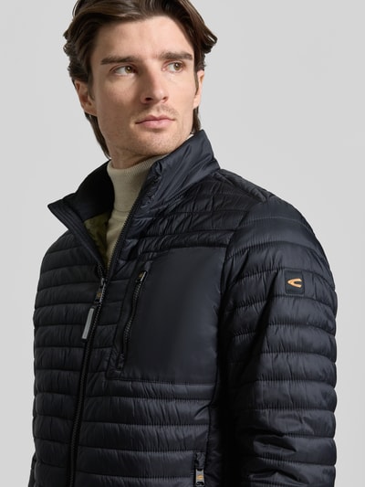 Männermodel trägt schwarze Steppjacke mit Stehkragen von camel active, Reißverschluss, Reißverschlusstaschen, Nahaufnahme Oberkörper.