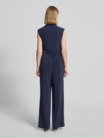 Frauenmodel trägt Jumpsuit in Wickel-Optik mit Schalkragen von Vera Mont in Dunkelblau, Material-Mix mit Stretch-Anteil, Taillierter Schnitt, Raffungen, Rückseitiger Reißverschluss, Rückenlänge 41 cm, Brustweite 45 cm, Ärmellänge 14 cm, Gesamtlänge 154 cm, Innenbeinlänge 86 cm, fließende Textur, Ganzkörperansicht Rückansicht.