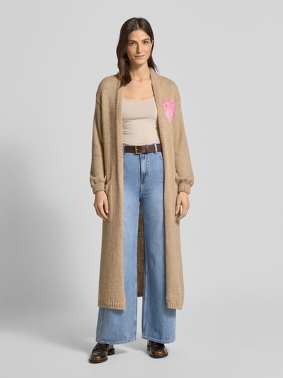 Frauenmodel trägt Longcardigan mit Eingrifftaschen von miss goodlife aus Baumwoll-Alpaka-Mix, beige, lockerer Schnitt, gerippte Abschlüsse, Ganzkörperansicht von vorne.