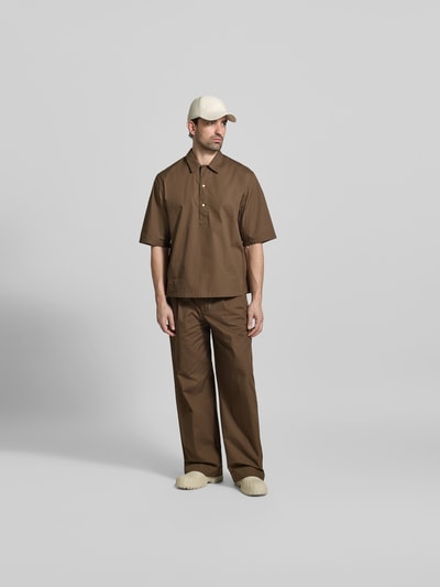 Männermodel trägt Relaxed Fit Freizeithemd mit Kentkragen von Officine Générale aus reiner Baumwolle, braun, mit Halbarm und Knopfleiste, Ganzkörperansicht von vorne. Rückenlänge bei Größe M: 74 cm, Schulterbreite 60 cm, Ärmellänge 33 cm.