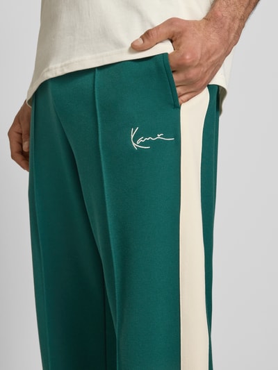Männermodel trägt Straight Fit Sweatpants mit Logo-Stitching van KARL KANI in groen met beige, elastische materiaalmix met katoen, detailaufnahme rechterzij.