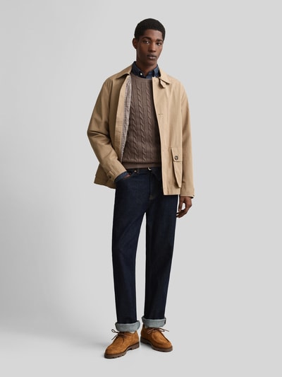 Männermodel trägt Regular Fit Pullover aus reiner Baumwolle von GANT in Braun mit Zopfstrickstruktur, Ganzkörperansicht von vorne.