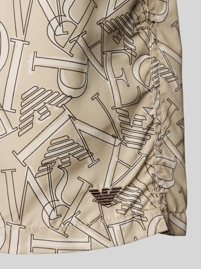 Produktfoto, Regular Fit Shorts mit Allover-Logo-Print von Emporio Armani in Beige mit braunem Logo-Print, glatte Textur, elastischer Bund, Detailaufnahme.
