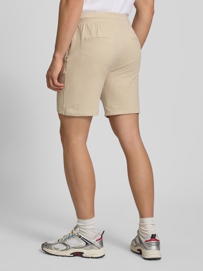 Männermodel trägt Loose Fit Sweatshorts aus Bio-Baumwoll-Mix Modell 'KIAN' von Only & Sons, beige, Piqué-Struktur, Ganzkörperansicht Rückansicht.
