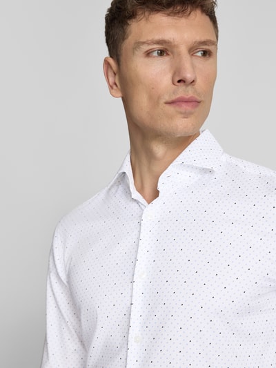 Mężczyzna nosi Regular Fit Businesshemd aus reiner Baumwolle von BOSS, efekt: wzór na całej powierzchni, kołnierzyk typu cutaway, listwa guzikowa na całej długości, długi rękaw z mankietem, materiał: bawełna; jasny kolor z drobnym wzorem, lekka faktura. Nahaufnahme górnej części ciała.