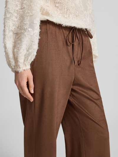 Frauenmodel trägt Wide Fit Stoffhose mit Gesäßtasche von Oui in Braun, elastischer Bund, leichte Stofftextur, Nahaufnahme Oberkörper.
