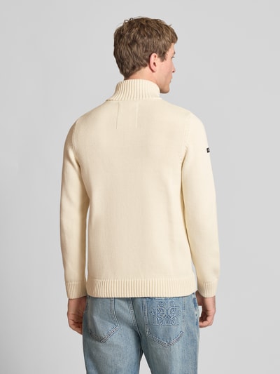 Männermodel trägt Slim Fit Pullover in Strick-Optik von Superdry, cremefarben, Stehkragen, Logo-Stitching, Ganzkörperansicht Rückansicht.