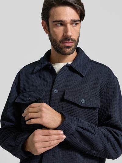 Männermodel trägt Hemdjacke mit Knopfleiste von MCNEAL, dunkles Blau, Material-Mix mit Viskose-Anteil, strukturierte Oberfläche, Nahaufnahme Oberkörper.