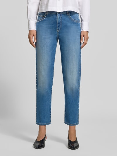 Kobieta nosi Slim Fit Jeans aus Baumwoll-Mix mit Nietenbesatz von Marc Cain, niebieskie, krój slim fit, obszycie nitami, skrócony krój, 5 kieszeni, zapięcie na guzik i zamek błyskawiczny, szerokość w rozmiarze 36: 40 cm, długość wewnętrzna nogawki w rozmiarze 36: 72 cm, mieszanka bawełny, widok całej sylwetki z przodu.