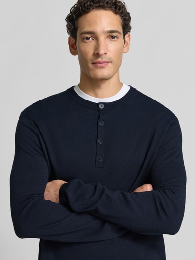 Männermodel trägt dunkelblauen Strickpullover mit Henley-Kragen von DRYKORN aus reiner Baumwolle, gerader Schnitt, Nahaufnahme Oberkörper.