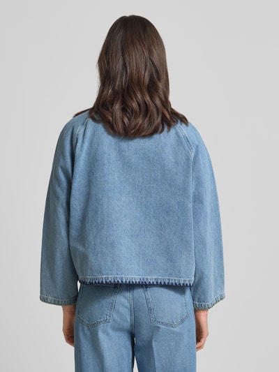 Kobiece model nosi kurtka jeansowa z haftem i kieszeniami z patką 'Jeansjacke mit Stitching und Pattentaschen' od Amber & June, wykonana z czystej bawełny, pudełkowy krój, wykładany kołnierz, średni niebieski kolor, długość tyłu w rozmiarze 36: 56 cm, szerokość ramion w rozmiarze 36: 46 cm, szerokość klatki piersiowej w rozmiarze 36: 63 cm, długość rękawów w rozmiarze 36: 55 cm, faktura materiału gładka, widoczne wykończenie szwem, widoczne szwy, zdjęcie całej sylwetki z tyłu.
