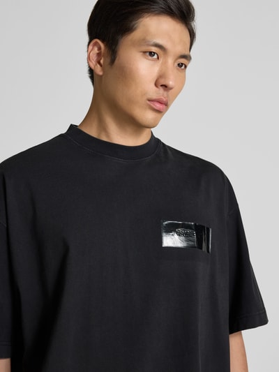 Männermodel trägt T-Shirt aus reiner Baumwolle von VETEMENTS in Schwarz mit Label-Detail, Relaxed-Fit, Rundhalsausschnitt, Nahaufnahme Oberkörper.