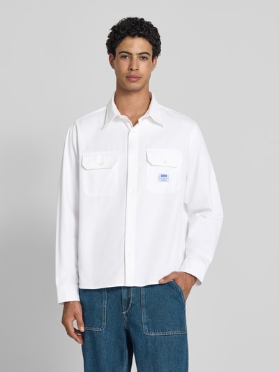 Męski model nosi Oversized Freizeithemd aus reiner Baumwolle Modell 'EKYNONE' od HUGO, jednokolorowy, splot twill, naszywka z logo, kołnierzyk typu kent, listwa guzikowa na całej długości, długi rękaw, sportowe mankiety, nakładane kieszenie na piersi, wykończenie: bawełna, Ganzkörperansicht von vorne.
