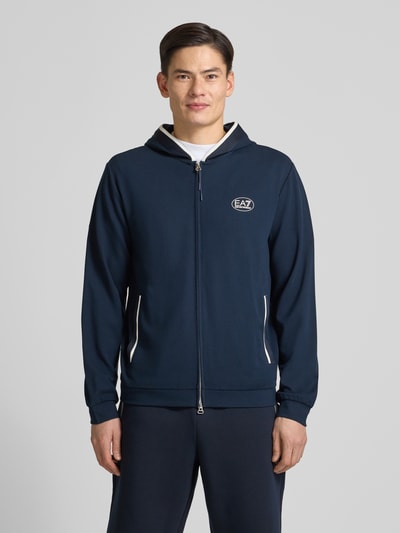 Męski model nosi Bluza rozpinana z logo i zamkiem błyskawicznym dwustronnym od Armani, mieszanka wiskozy, krój regular fit, wpuszczane kieszenie, kaptur, granatowy kolor, długość tyłu 68 cm, długość rękawów 68 cm, całkowity widok z przodu.