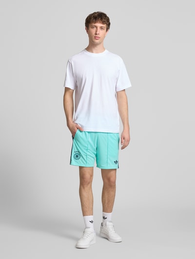Männermodel trägt Auswärtsshorts Deutschland 2026 von adidas, mehrfarbig, Passform: Regular-Fit, Bundabschluss: Tunnelzug, Ganzkörperansicht von vorne.