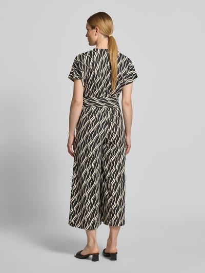 Frauenmodel trägt Jumpsuit im Allover-Look mit V-Ausschnitt von Betty Barclay, schwarz-beige gemustert, Material-Mix mit Stretch, Ganzkörperansicht Rückansicht.