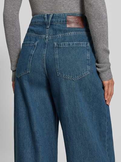 Frauenmodel trägt Wide Fit Jeans mit gelegten Falten von MYON aus reiner Baumwolle, blaue Denim-Struktur, Nahaufnahme Rückansicht.
