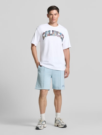 Männermodel trägt T-Shirt mit 1/2-Arm von COLUCCI, weiß, bunte Schrift, reine Baumwolle, gerader Schnitt, Rundhalsausschnitt, Ganzkörperansicht von vorne.