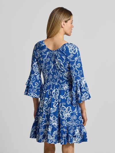 Frauenmodel trägt Minikleid aus reiner Viskose mit Smok-Detail von Apricot mit floralem Allover-Print in Blau und Weiß, Rüschenbesatz, tailliert, 3/4-Arm, V-Ausschnitt, Rückenansicht Ganzkörperansicht.