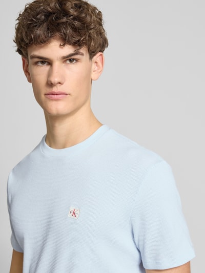 Männermodel trägt Regular Fit T-Shirt mit Logo-Patch von Calvin Klein Jeans aus Baumwoll-Mix mit Strukturmuster, Nahaufnahme Oberkörper.