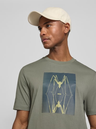 Männermodel trägt Regular Fit T-Shirt aus reiner Baumwolle Modell 'TE_CREATURE' von BOSS Orange in Khaki, Motiv-Print, Nahaufnahme Oberkörper.