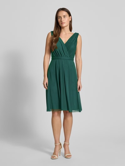 Frauenmodel trägt Cocktailkleid mit V-Ausschnitt von TROYDEN COLLECTION in Dunkelgrün, taillierter Schnitt, Ganzkörperansicht von vorne.