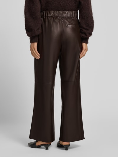 Vrouwenmodel draagt Wide Fit broek in leerlook van comma, donkerbruin, elastische band, steekzakken, bandwijdte 40 cm, binnenbeenlengte 75 cm, wide fit dames, leren textuur, volledig lichaam achteraanzicht