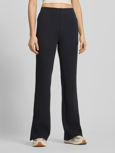 Kobiece model nosi Flared Sweatpants mit Logo od adidas Sportswear z mieszanki materiałów z domieszką modalu, rozkloszowany krój, elastyczny pas, logo, długość wewnętrzna nogawki 82 cm, kolor czarny, gładka tekstura.  Całkowity widok z przodu.