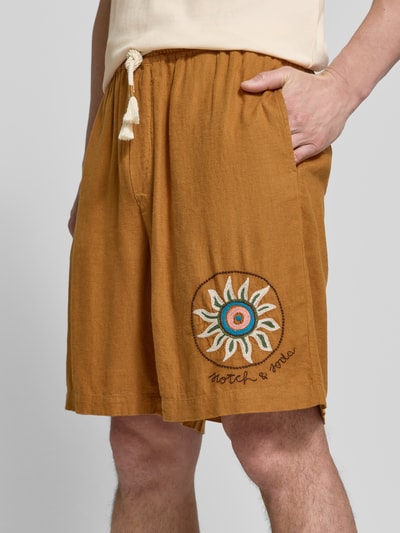 Männermodel trägt Straight Fit Shorts aus Leinen-Viskose-Mix mit Motiv-Stitching von Scotch & Soda, Logo-Stitching, elastischer Bund mit Tunnelzug, Nahaufnahme Oberschenkel.