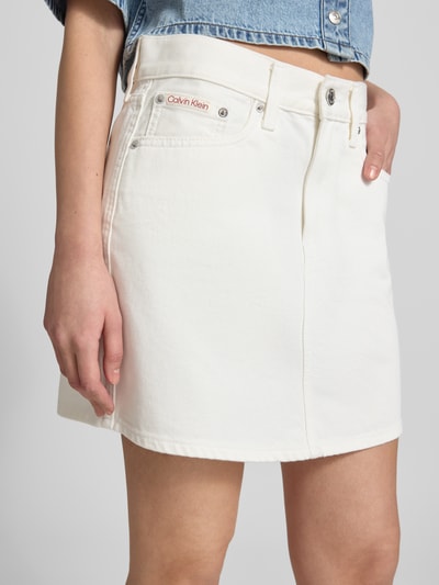 Vrouwenmodel draagt jeansrok im 5-pocketmodel model '90S' van Calvin Klein Jeans met katoenmix in wit, labeldetail, mini-jurk, straight fit, knoop- en ritssluiting, totale lengte maat 27: 40 cm, bandwijdte maat 27: 40 cm, nahaufnahme bovenbeen.