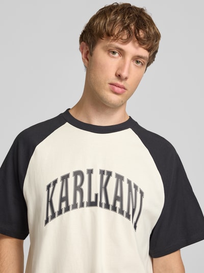 Männermodel trägt Boxy Fit T-Shirt mit Label-Print von Karl Kani in Schwarz-Weiß, Reine Baumwolle, Rundhalsausschnitt, Nahaufnahme Oberkörper.