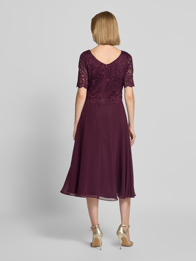 Frauenmodel trägt Tailliertes Cocktailkleid mit Spitzenbesatz von Vera Mont in dunklem Lila, fließender Stoff, Rückansicht Ganzkörperansicht.