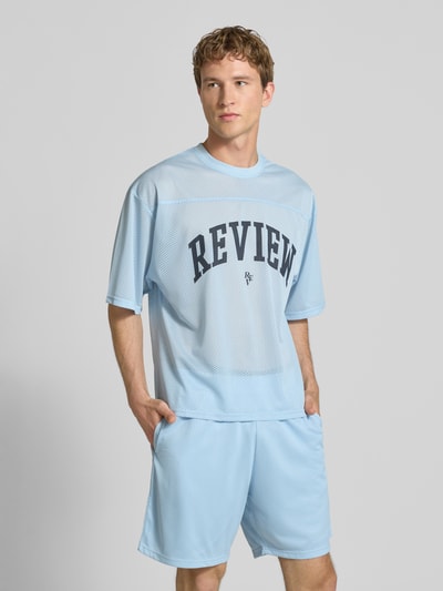 Männermodel trägt T-Shirt aus Mesh mit Logo-Print von REVIEW in Hellblau, Loose-Fit, Rundhalsausschnitt, Rückenlänge 66 cm bei Größe M, Ganzkörperansicht von vorne.