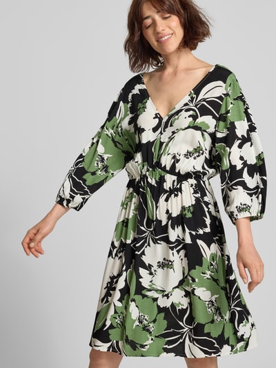 Frauenmodel trägt Knielanges Kleid aus Viskose im Allover-Look Modell 'Fe44li' von ZABAIONE in Grün, Schwarz und Weiß, A-Linie, V-Ausschnitt, 3/4-Arm, fließende Textur, Ganzkörperansicht von vorne.