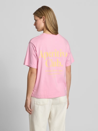Frauenmodel trägt Damen T-Shirt mit Statement-Print Modell 'SENNA' von JJXX aus reiner Baumwolle, Loose-Fit, Rückenlänge 60 cm, Ganzkörperansicht Rückansicht.
