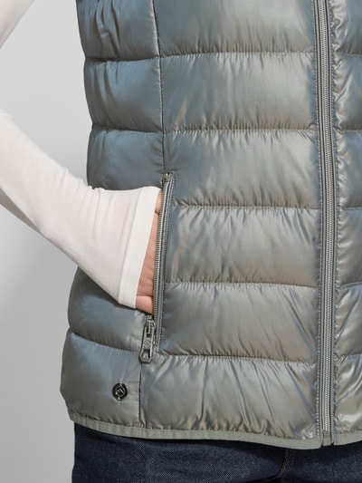 Vrouwenmodel draagt Steppweste mit Stehkragen van NAUTGÅRD in regular fit met ritssluiting en ritszakken, detailopname rechterzij. Ruglengte maat S: 64 cm, schouderbreedte: 35 cm, borstwijdte: 46 cm.