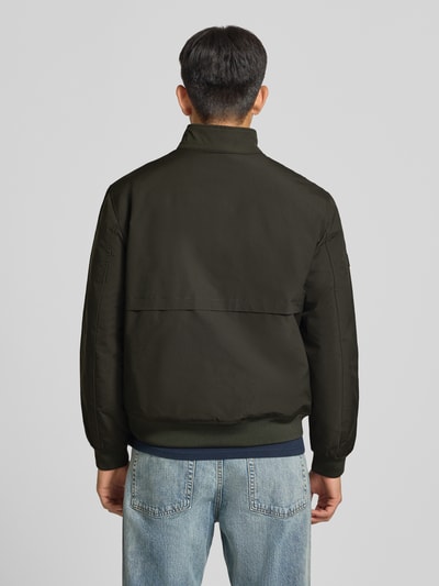 Männermodel trägt Regular Fit Jacke mit Logo-Stitching Modell 'HARRINGTON' von Superdry, dunkelgrün, glatte Textur, Ganzkörperansicht Rückansicht. Elastischer Material-Mix, Stehkragen, Reißverschluss, Rückenlänge bei Größe M 66 cm, Schulterbreite 50 cm, Brustweite 60 cm, Ärmellänge 65 cm.