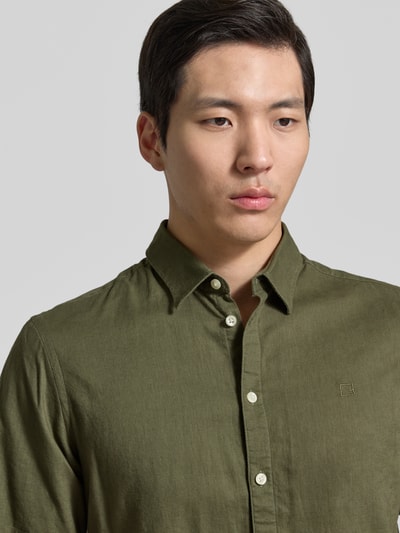 Männermodel trägt Slim Fit Freizeithemd aus Leinen-Baumwoll-Mix Modell 'AKSEL' von Casual Friday in olivgrün, Nahaufnahme Oberkörper, Kentkraag, label-stitching, knopenlijst, ruglengte 78 cm, schouderbreedte 45 cm, mouwlengte 27 cm.